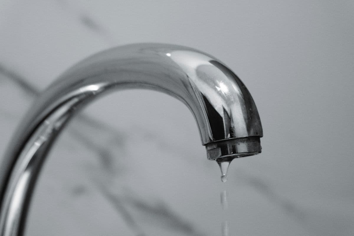 Hand turning a residential faucet with no water coming out, indicating a well pump failure.